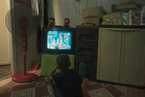 Six-year-old Youssef is watching television with a fan on, which he could do only at night.